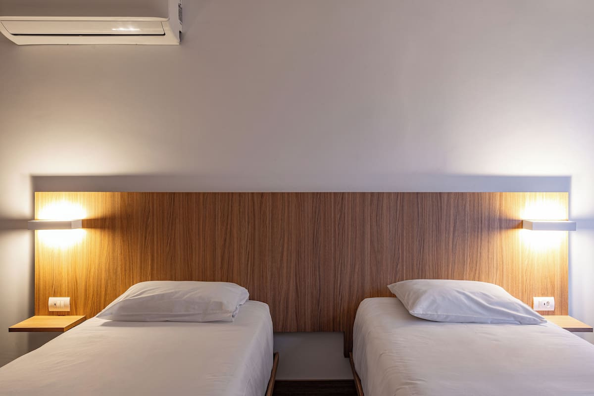 A double room with two beds, wooden headboard, bedside lamps, and a small shelf.