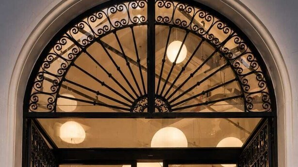 L’entrée d’un hôtel, avec un comptoir d’accueil, une grande porte en arc de cercle et des lampes sphériques suspendues.