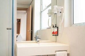 Un baño con lavamanos blanco, un espejo, secador de pelo y un toallero.