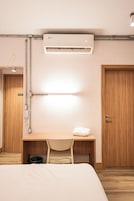 Una camera d'albergo con un letto, una scrivania con una sedia, un condizionatore d'aria, un telefono e una porta.