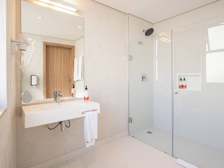 A modern bathroom with a glass shower enclosure, a white sink with a mirror, and a hairdryer mounted on the wall.