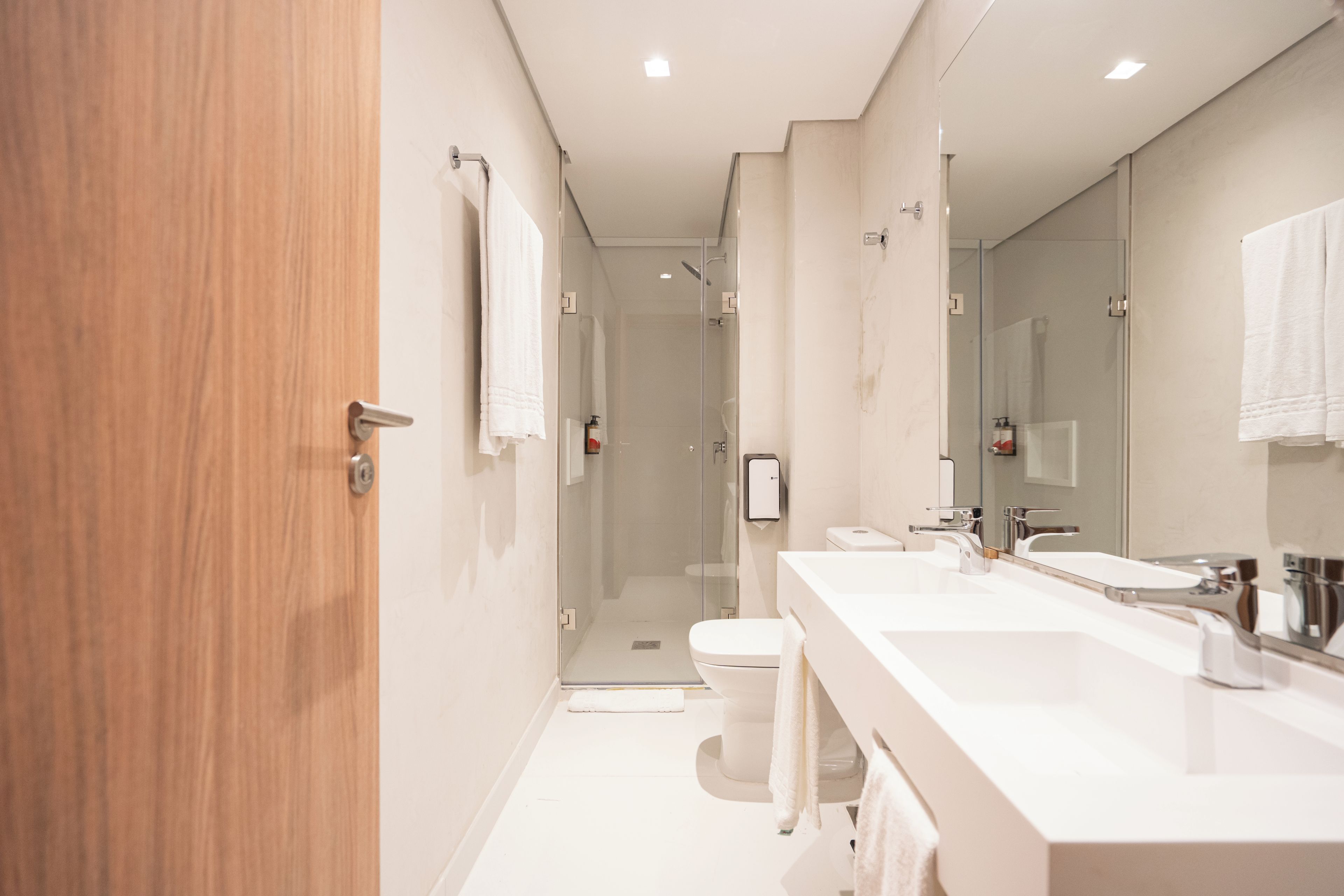 A modern bathroom with a wooden door, a glass shower enclosure, and a white sink with a mirror.