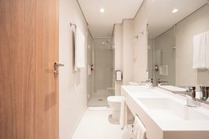 A modern bathroom with a wooden door, a glass shower enclosure, and a white sink with a mirror.