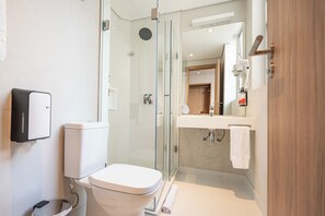 A modern bathroom with a toilet, a glass-enclosed shower, a sink with a mirror, and a towel rack.