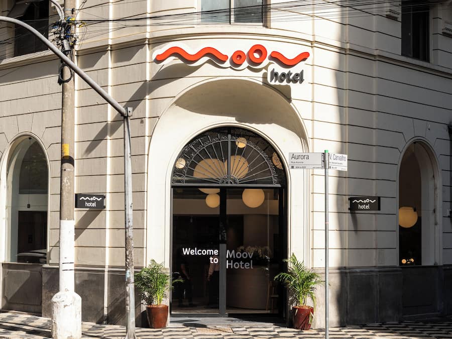 Entrada de hotel com fachada curva, uma grande porta em arco e um letreiro sobre a entrada.