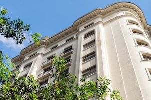 Um edifício de vários andares com características arquitetônicas clássicas, incluindo uma varanda no segundo andar e uma série de janelas em cada pavimento.