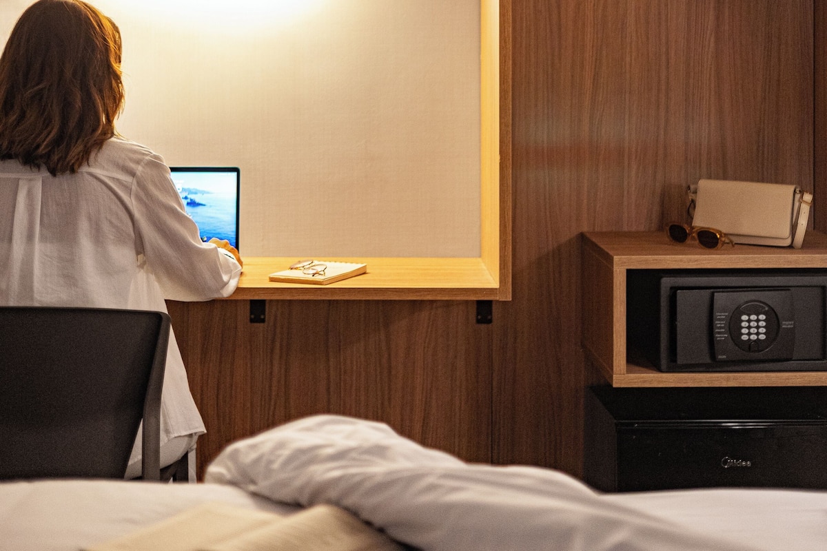 A hotel room with a bed, a desk with a computer, a wooden wardrobe, and a microwave.