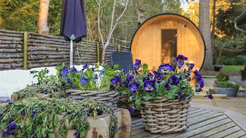 A rustic outdoor setting with a wooden barrel, wicker baskets with flowers, and a wooden table.