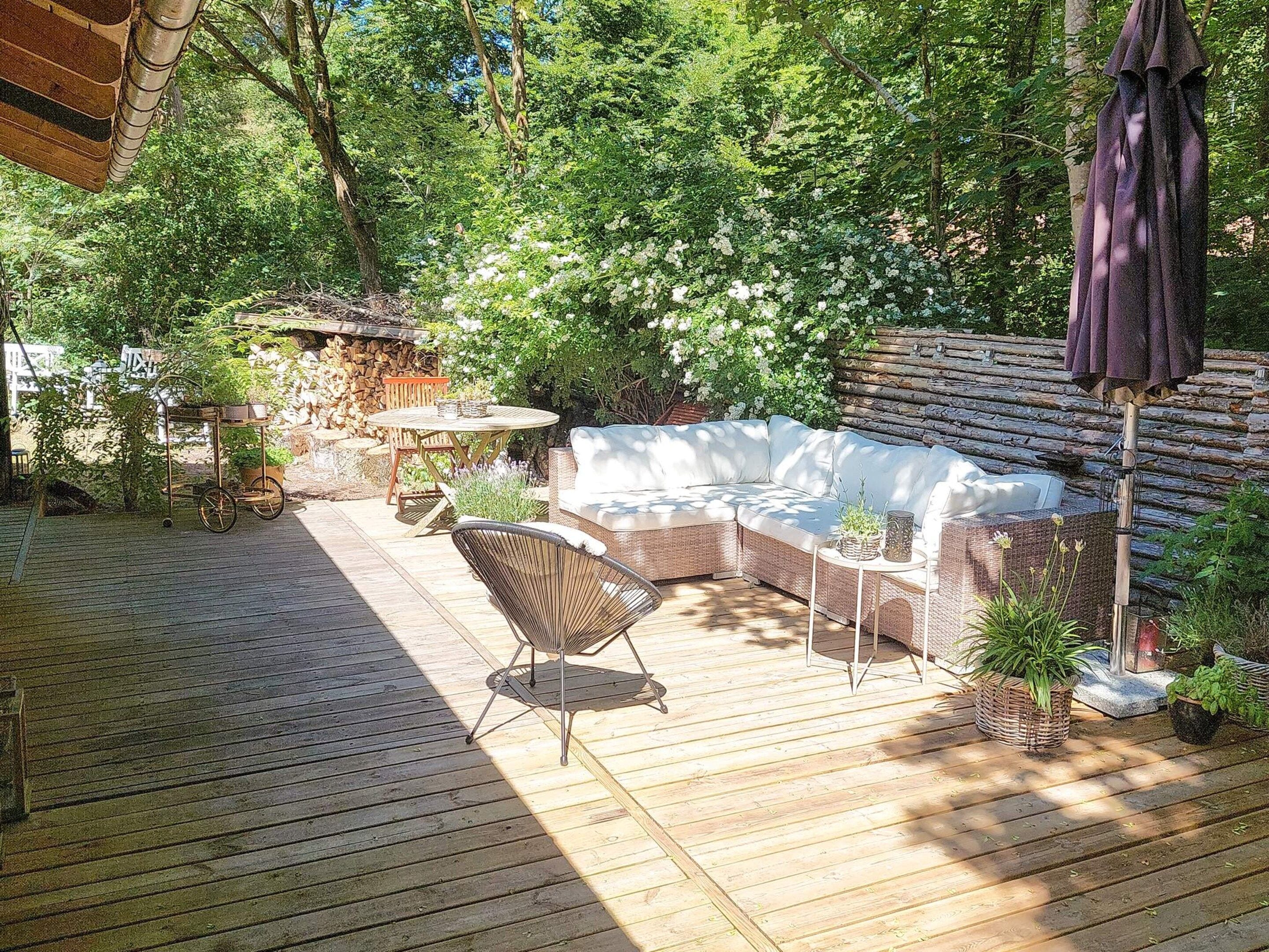 A wooden deck with a wicker sofa, a round table, and a chair.