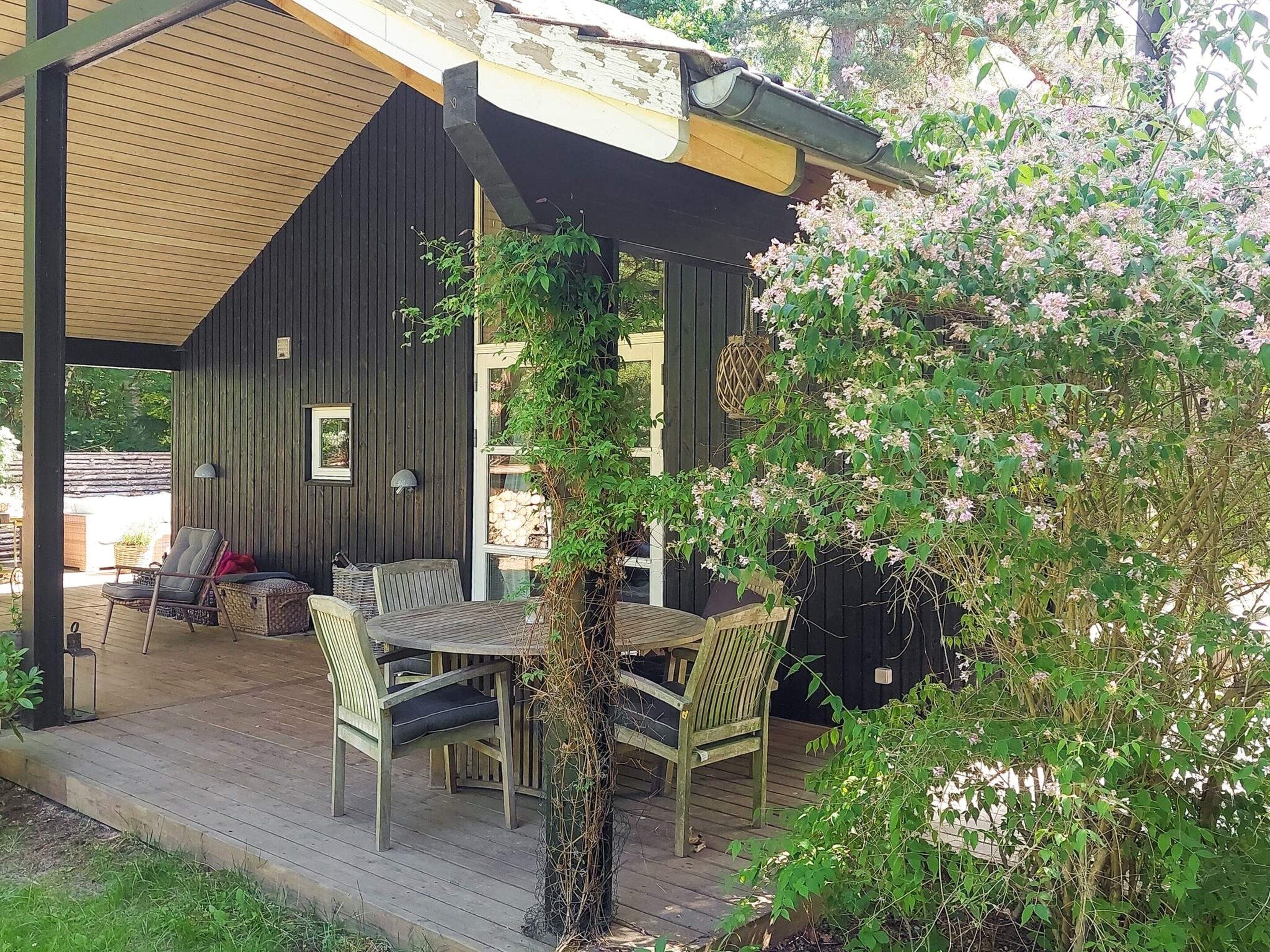 A wooden deck with outdoor furniture, a covered seating area, and a garden with flowering plants.