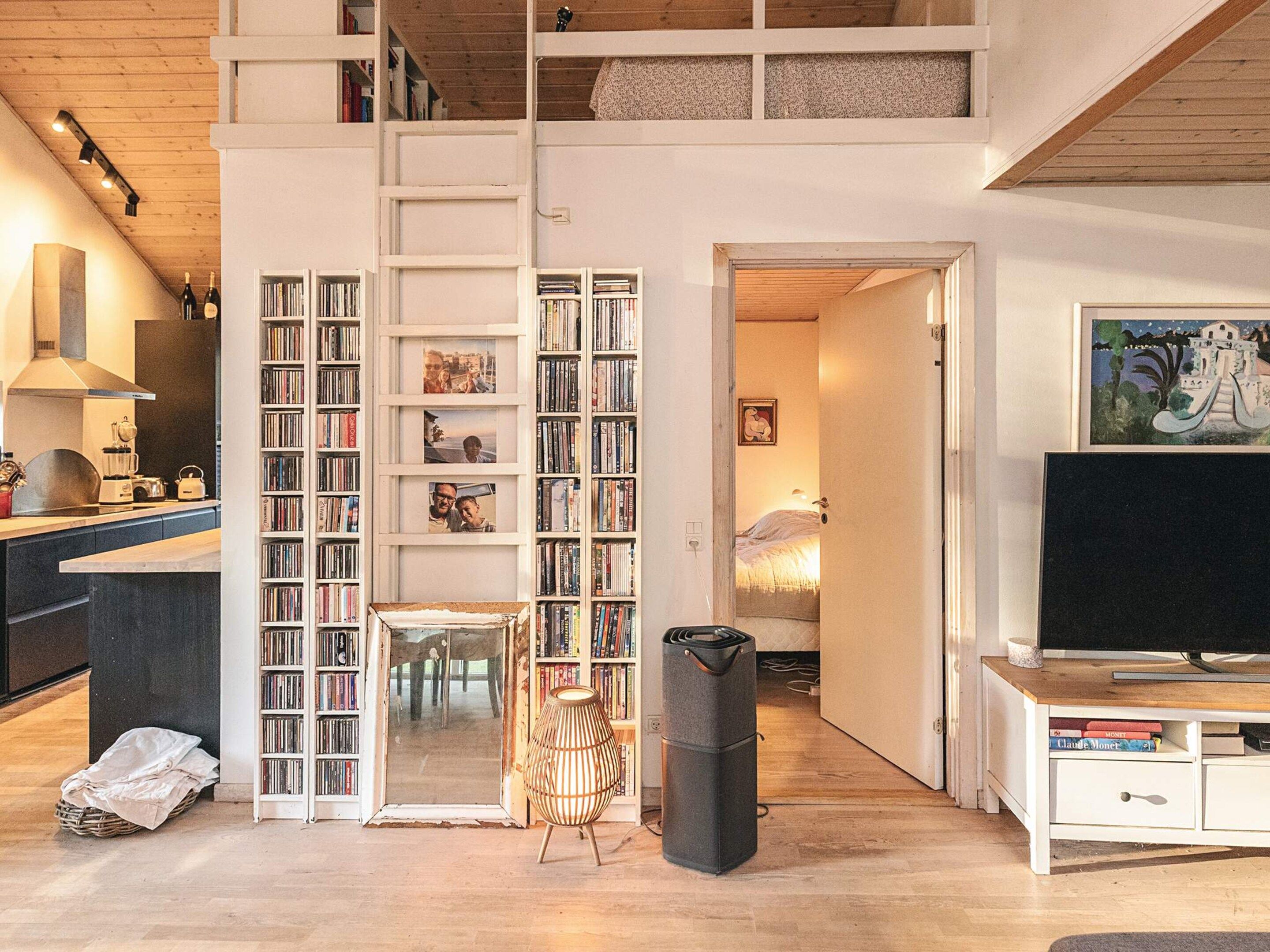 Un espacio habitable en varios niveles, con área de cocina, estante para libros, televisor y comedor.