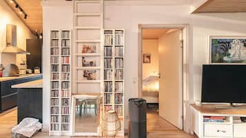 Un espacio habitable en varios niveles, con área de cocina, estante para libros, televisor y comedor.
