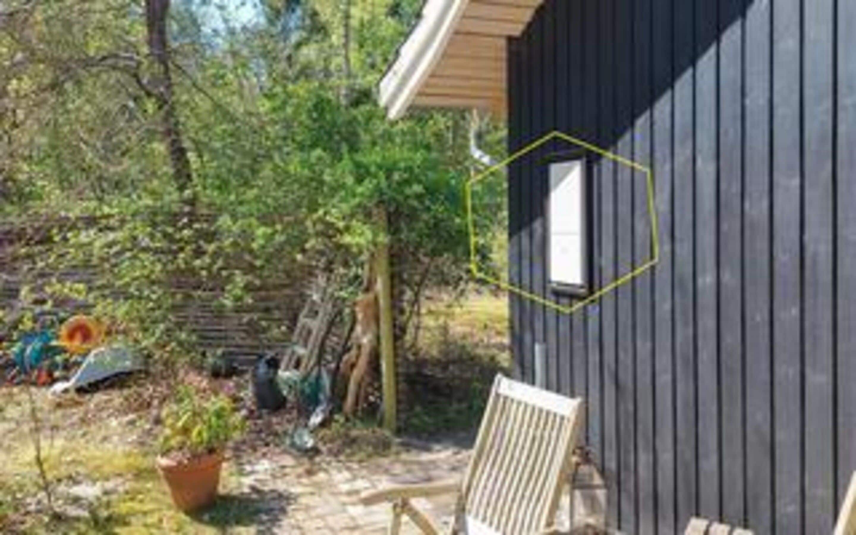 Una cabaña de madera con ventana, rodeada de árboles y un jardín.