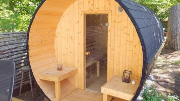 A wooden sauna with a bench and a table, a door, and a small table with a candle.