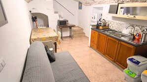 Un espacio habitable compacto con sofá, una pequeña mesa de comedor, una zona de cocina con armarios y un lavabo, y una escalera que sube a un nivel superior.