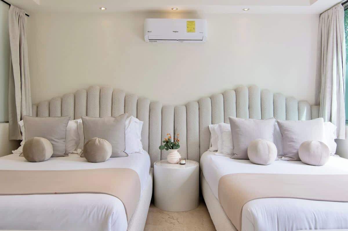 Habitación de hotel con dos camas, una mesita redonda, aire acondicionado instalado en la pared y una ventana con cortinas.