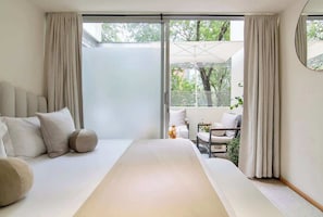 Ein Schlafzimmer mit einem großen Bett, einem Schlafsofa und Blick auf einen Balkon mit Gartenmöbeln.