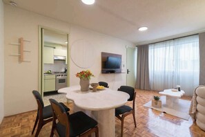 A living room with a round table, chairs, a TV mounted on the wall, and a kitchen visible through an open door. - Mexican 2BR - 2Bath of Condesa - Wifi High Speed (Mexico City)