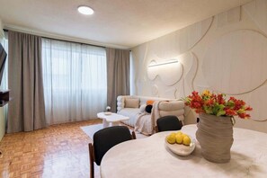 A modern living room with a sofa, a dining table with a vase of flowers, and a flat-screen TV. - Mexican 2BR - 2Bath of Condesa - Wifi High Speed (Mexico City)