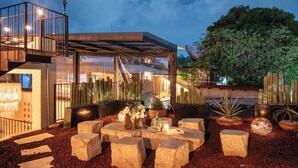En moderne udendørs terrasse med stenbænke, kaktusser og en glasstruktur.