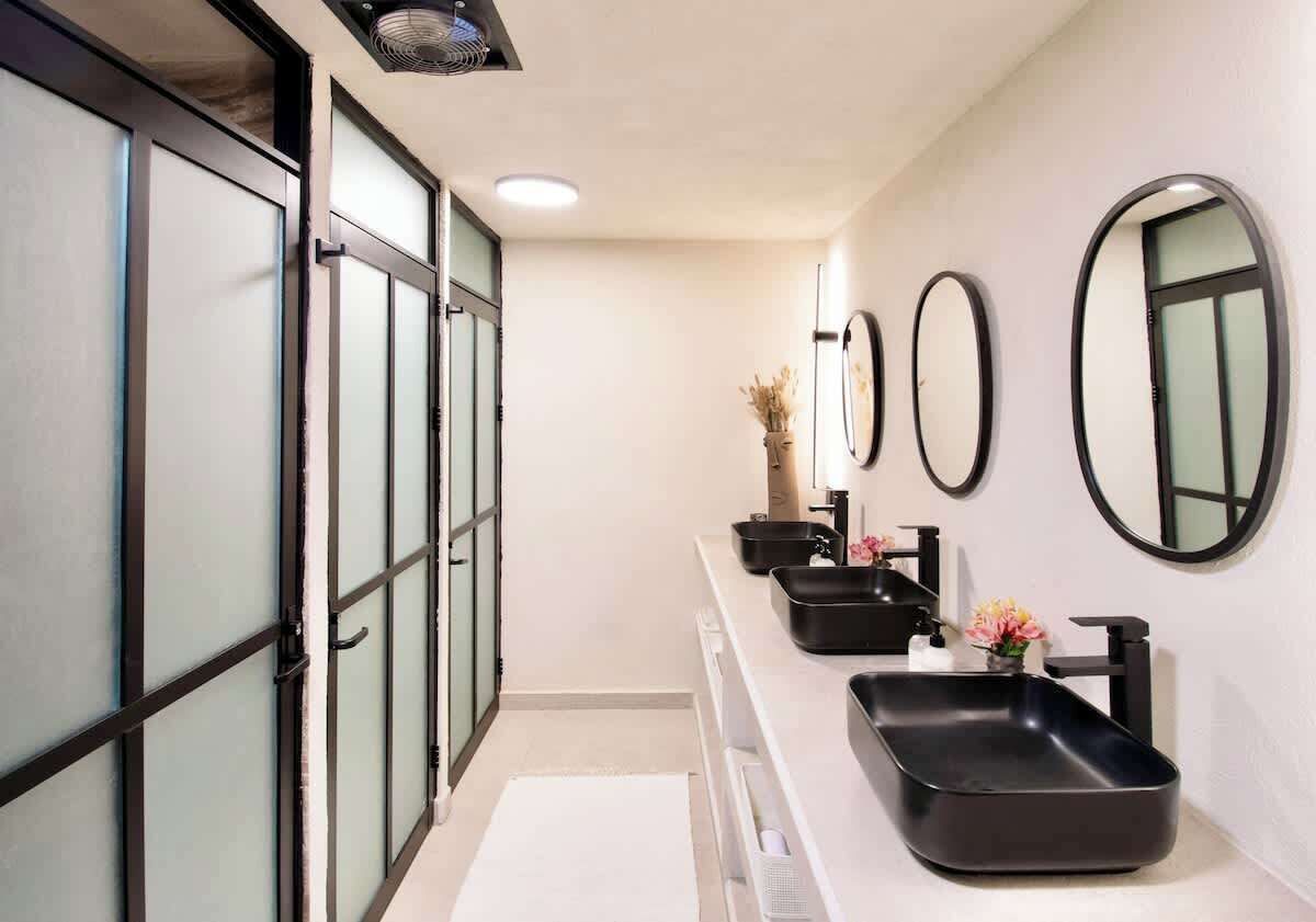 A modern bathroom with a long vanity, black sinks, and multiple mirrors.