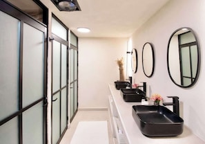 Un bagno moderno con un lungo piano da bagno, lavabi neri e numerosi specchi.