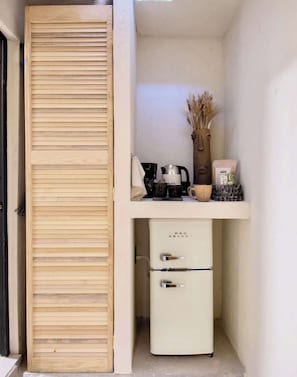 Un angolo cottura compatto con una porta scorrevole in legno, un frigorifero vintage in velluto rosso, una moka e un vaso con piante essiccate.