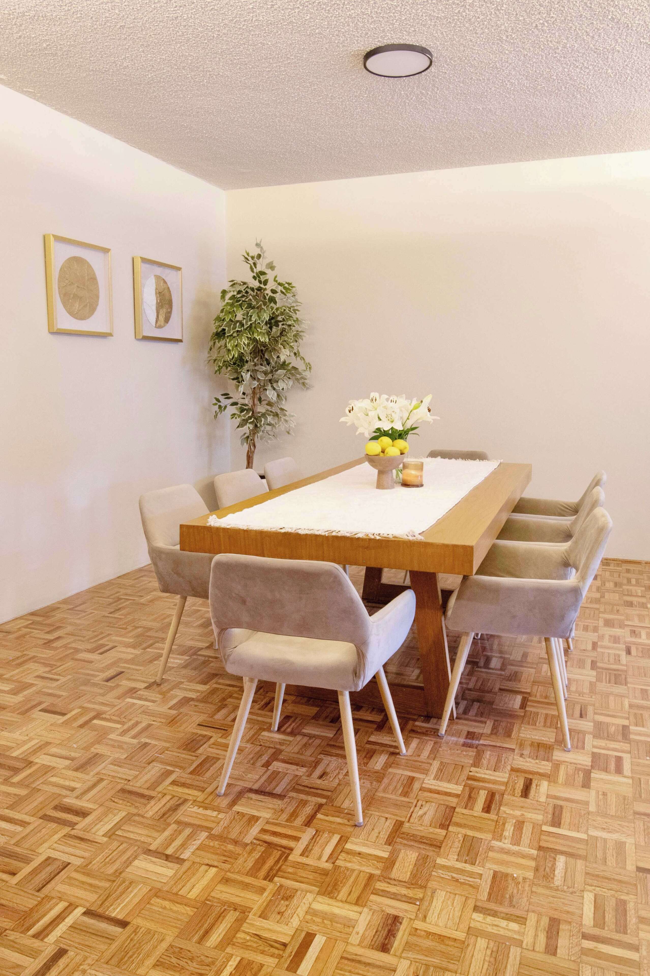 Un coin repas avec une table en bois, des chaises à revêtement gris, une plante en pot et des œuvres d’art encadrées accrochées au mur.