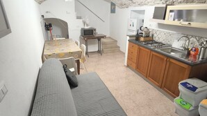 A compact living space with a sofa, a dining table, a kitchen area with cabinets and a sink, and a staircase leading to an upper level. - Room 'Fichi D'India' with Wi-Fi and Air Conditioning (Modugno)