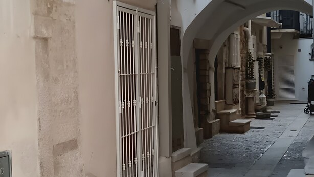 A narrow street with a row of buildings, a gated entrance, and a small archway. - Room 'Fichi D'India' with Wi-Fi and Air Conditioning (Modugno)