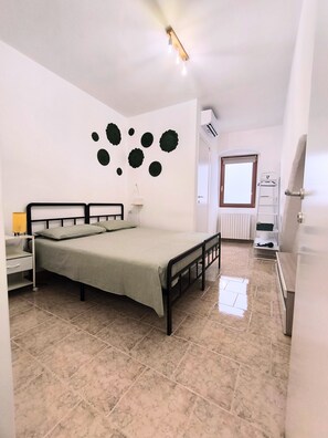 Una camera da letto con un letto, un comodino, una lampada, un elemento decorativo a parete, un termosifone e una porta.
