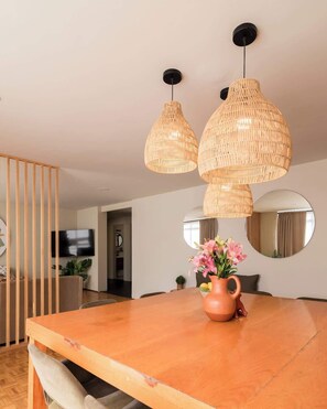 A dining area with a wooden table, a vase with flowers, and three woven pendant lights. - Chic Stylish Design Flat in Roma Norte Prime Area (Mexico City)