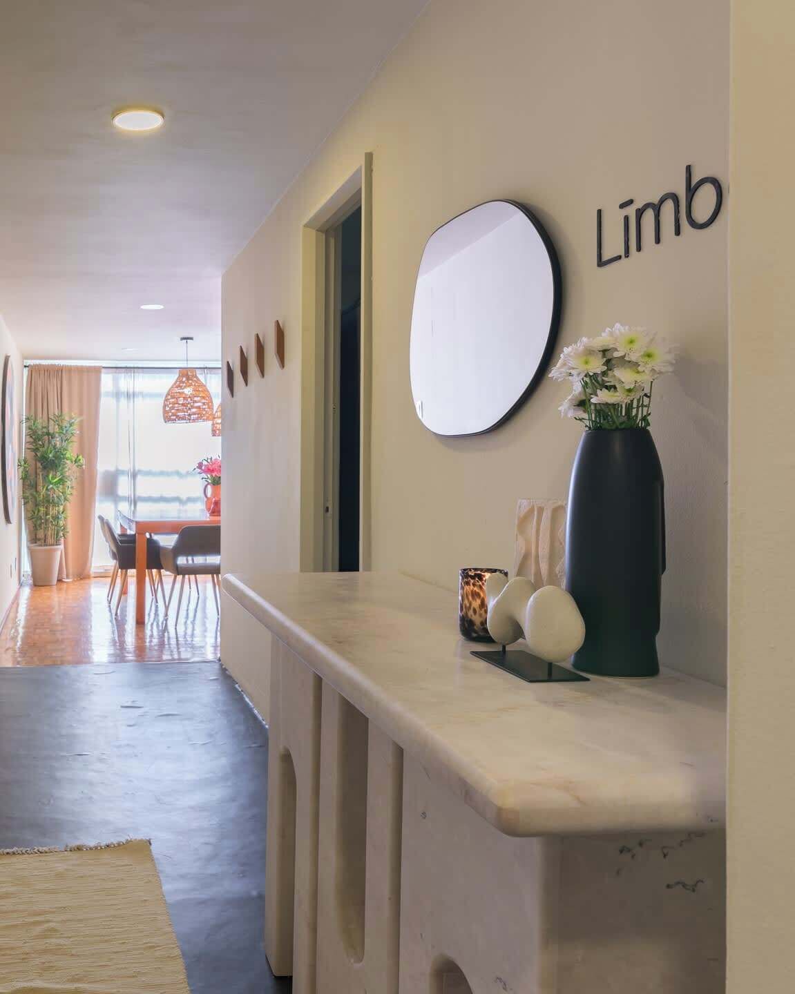 A hallway with a reception desk, a round mirror, a vase with flowers, and a sign that reads 'Limb.'