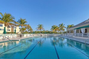 Ein klares, blaues Schwimmbecken mit Liegestühlen und Palmen, umgeben von Gebäuden.