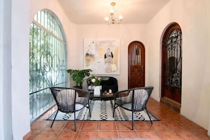 A dining area with a table, chairs, a chandelier, a fireplace, and a large window with decorative ironwork.