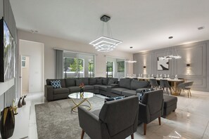 Ein modernes Wohnzimmer mit einer Eckcouch, einem Glastisch und einem Essbereich mit rundem Tisch und Stühlen.