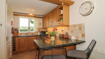 Una cocina con armarios de madera, un microondas integrado, una ventana y un reloj de pared.