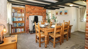 A dining area with a brick fireplace, wooden table, chairs, and a bookshelf. - Fron-haul (Llansantffraid-ym-Mechain)