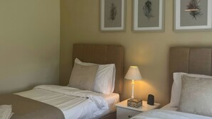 Una habitació d'hotel amb dos llits, una vetusta amb una làmpada, i tres obres d'art amb plomes a la paret.