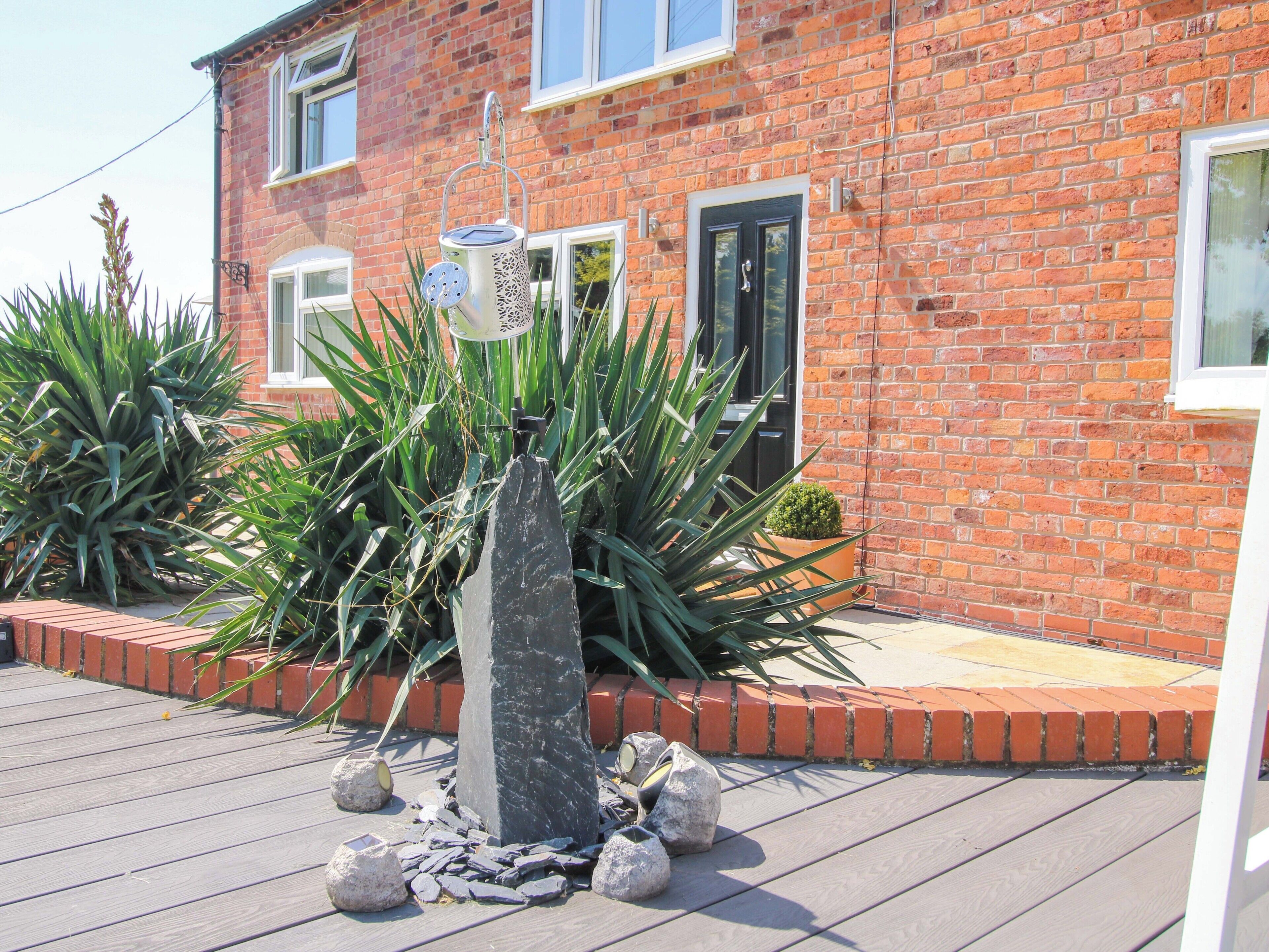 A brick house with a garden featuring a rock centerpiece and various plants.