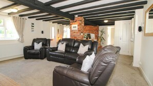 A living room with a fireplace, leather sofas, and exposed wooden beams. - Fron-haul (Llansantffraid-ym-Mechain)