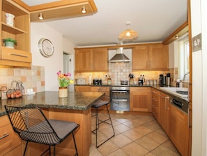 A modern kitchen with wooden cabinets, a built-in oven, a coffee maker, and a clock on the wall. - Fron-haul (Llansantffraid-ym-Mechain)