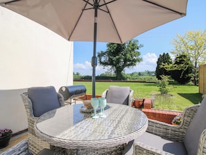 A round wicker table with chairs, a grill, and a table umbrella.