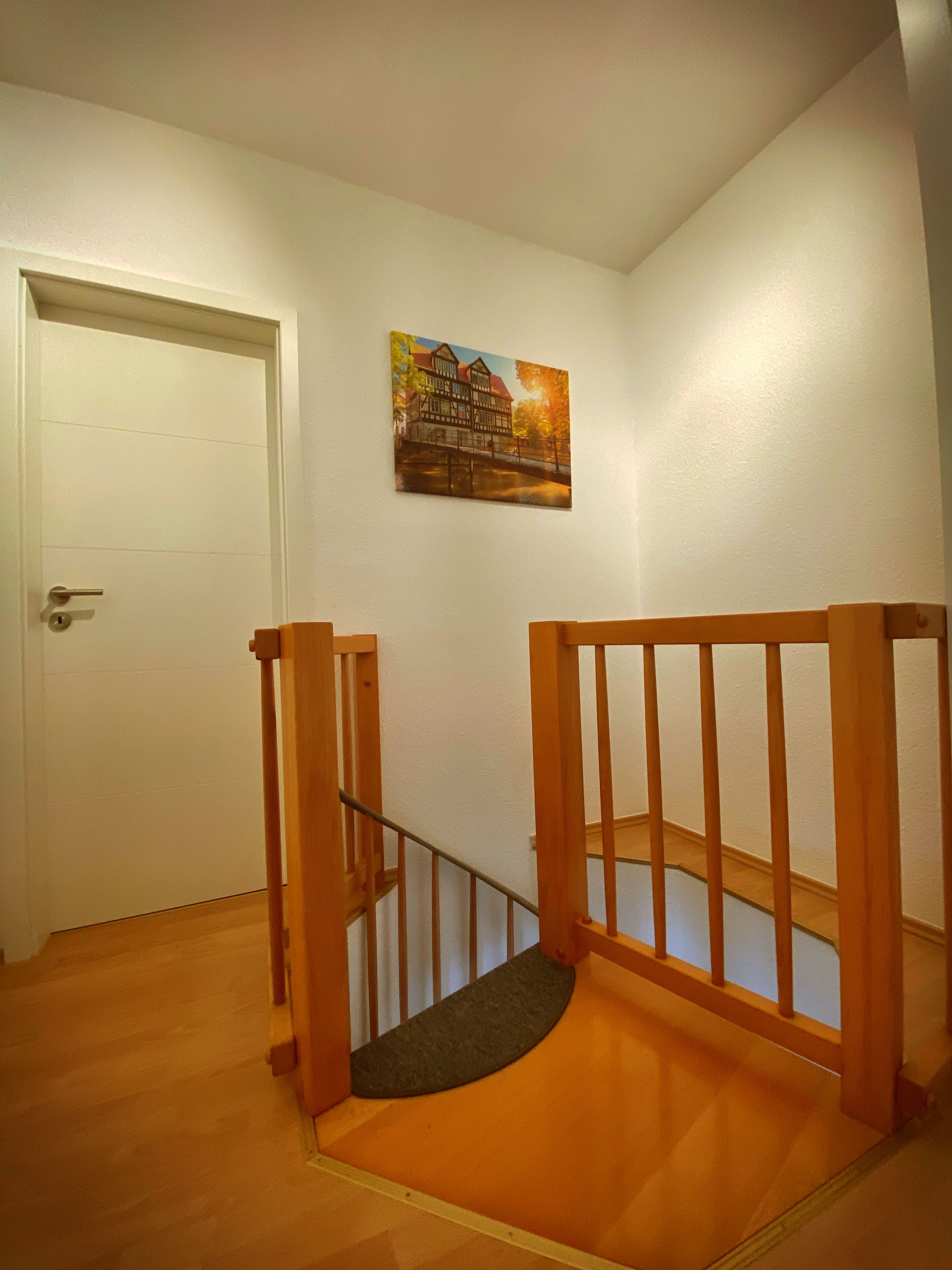 Una escalera con barandillas de madera, una puerta y un cuadro colgado en la pared.