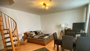 A modern living room with a staircase, a sofa set, a dining table with chairs, and a television. - Apartment at the ford (Erfurt)