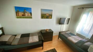 Un dormitorio con dos camas individuales, televisión, escritorio y dos cuadros colgados en la pared.