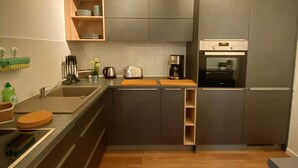A modern kitchen with grey cabinets, a wooden countertop, a built-in oven, and a ceiling light fixture. - Apartment at the ford (Erfurt)