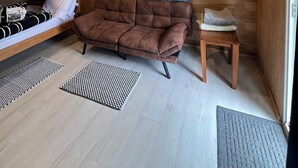 Interior de una cabaña de madera con literas, un sofá, una mesita y dos ventanas.