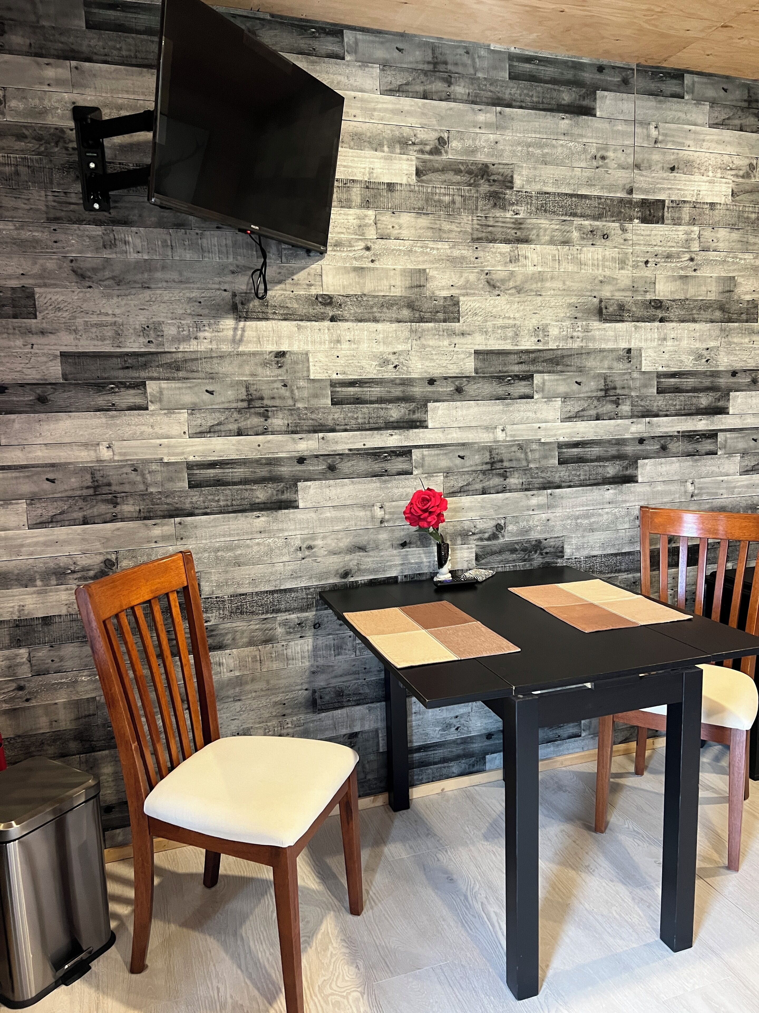 A dining area with a wooden wall, a TV mounted above a table, and chairs.