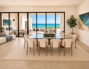 A modern living room with a glass table and chairs, a sofa, and a view of the ocean. - Casa Mar Bimini Beach Villa – Rockwell (North Bimini)